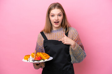 Teenager Russian girl holding a waffles isolated on pink background with surprise facial expression