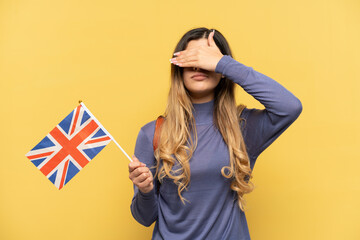 Young Russian girl holding an United Kingdom flag isolated on yellow background covering eyes by...