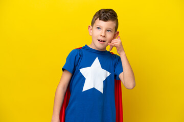 Little caucasian boy isolated on yellow background in superhero costume and doing phone gesture © luismolinero