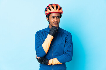Young cyclist man with braids over isolated background having doubts and thinking