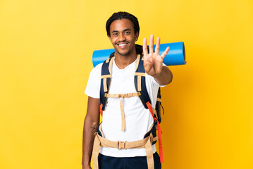 Young mountaineer man with braids with a big backpack isolated on yellow background happy and counting four with fingers