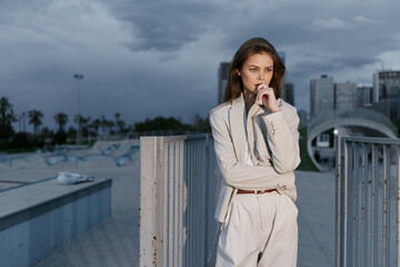 Fototapeta premium Thoughtful woman in beige business suit standing outdoors with cityscape and cloudy sky, expressing focus and contemplation