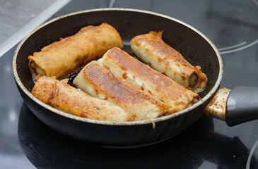Warm rolled crepes cooking in a frying pan on a stovetop at home, filled with savory or sweet ingredients in afternoon light