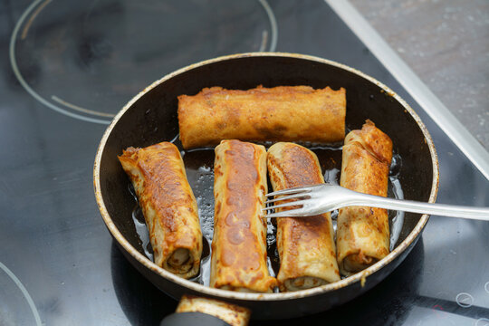 Cooked spring rolls in a frying pan browning on the stovetop in a kitchen setting during midday cooking preparations