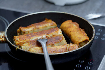 Cooking crispy rolled dumplings in a pan on a stovetop in a modern kitchen