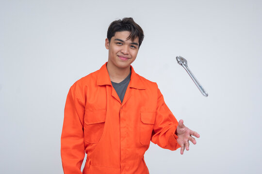 Relaxed Southeast Asian mechanic in orange coveralls tossing a wrench mid-air, expressing confidence and a casual attitude. Isolated on a light background.