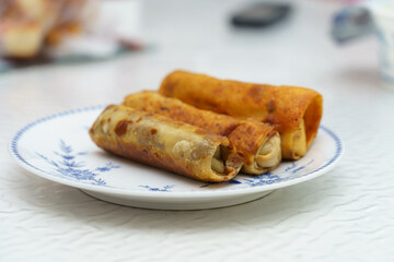 Three flavorful spring rolls served on a white plate with intricate blue patterns, perfect for an appetizing snack or appetizer