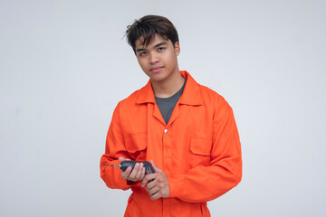 Young Southeast Asian male repair technician in orange uniform calmly holding an electric drill,...