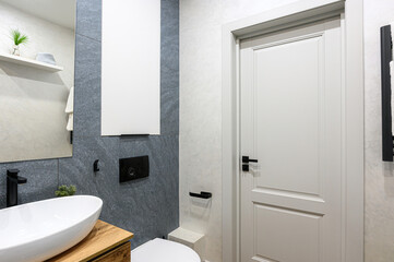 modern bathroom features a white vessel sink on a wooden cabinet, gray stone tiles, a white door with black hardware, and minimalist decor for a clean, elegant look.
