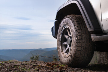 The concept of road trips and adventure tours on SUVs and cars in nature. A large wheel of an SUV on top of a mountain in close-up against the sky and space, the spirit of freedom.