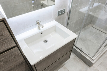 Modern bathroom featuring a white basin atop a wood-grain vanity, chrome faucet, and a tiled shower area.