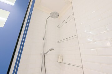 bright, clean shower area features white tiled walls, glass shelves, and a modern silver shower...