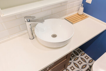 modern bathroom features a round white sink with a chrome faucet on a white countertop. White subway tiles line the wall, and a blue wall complements the patterned floor