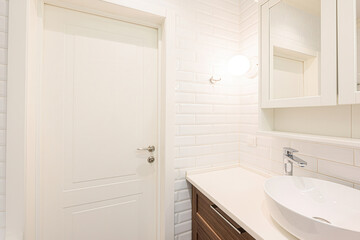 bright bathroom features white subway tiles, a white door, a modern sink on a wooden vanity, and a...