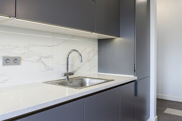 Modern kitchen detail.  Gray cabinets, stainless sink, marble backsplash, and bright countertop
