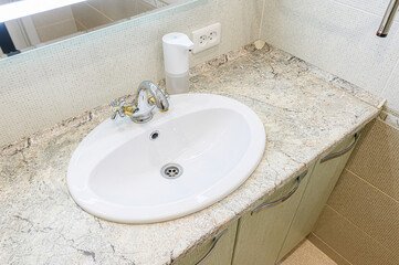 bathroom sink with a white oval basin, chrome faucet, automatic soap dispenser, and a marbled countertop.