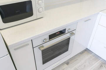 Fototapeta premium pristine white kitchen corner featuring a microwave and built-in oven set against a speckled countertop and sleek white cabinets.
