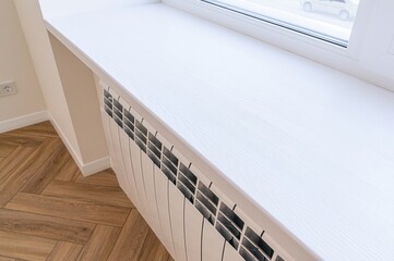 close-up shot showcases a pristine white windowsill above a radiator in a room with herringbone...