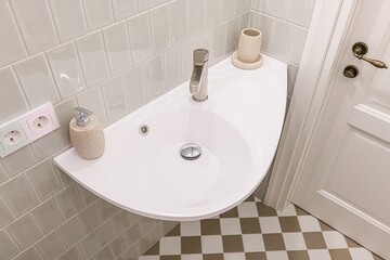 top-down shot of a bathroom corner with a modern white sink, light grey tiled walls, a checkerboard floor, and a white door with a brass handle