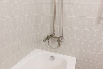 Close-up of a bathroom with a white tub, gray tiles, and a metal shower faucet