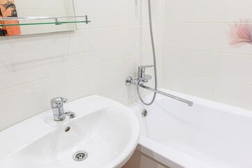 Clean bathroom interior. White tiled walls, sink, and bathtub. Chrome fixtures. Mirror and decorative flower detail.