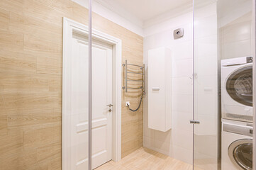 Bright bathroom with wood-look tile, white door, cabinet, and stacked washer/dryer visible through glass. Clean lines, modern design