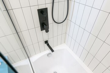 Clean bathroom corner featuring white tiled walls, black fixtures, and a white bathtub. The focus...