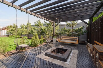 cozy backyard patio featuring a dark wood pergola, comfortable swing chairs, a fire pit surrounded...