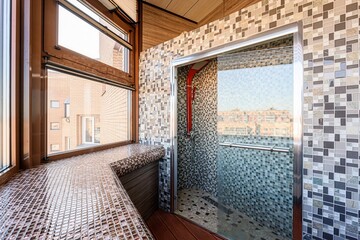 Modern bathroom featuring mosaic tiles, a glass shower stall, and a large window with a tiled sill.