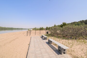 serene beach scene with calm waters, a sandy shore, and benches along a paved path. Exercise...