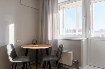 cozy dining nook with a round table, two grey chairs, and a window with cityscape view. Light streams in.