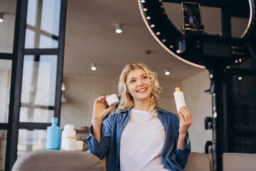 Happy teenager blogger holding cosmetics products while recording video stream at home