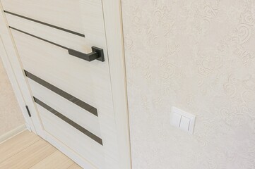 Interior shot featuring a modern light wood door with black accents next to a patterned beige wall...