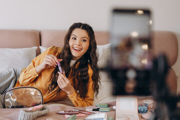 Young female makeup artist doing video blog about cosmetics in bedroom at home