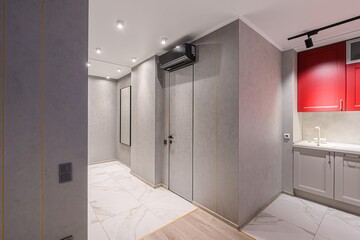 Modern hallway with gray walls accented by thin gold lines, marble tile flooring, and a red kitchen corner. Minimalist design.