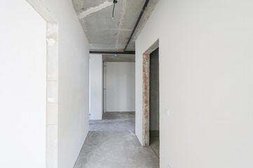 Fototapeta premium empty, unfinished room with white walls and a concrete floor. Pipes run along a concrete ceiling