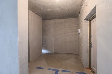 Bare, light-filled room in renovation with exposed concrete ceiling, plastered walls, and smooth...