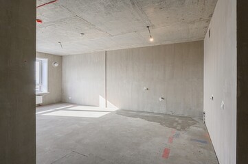 Bare, light-filled room in renovation with exposed concrete ceiling, plastered walls, and smooth concrete floor