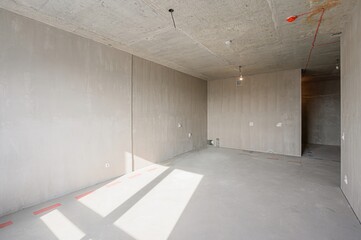 Bare, light-filled room in renovation with exposed concrete ceiling, plastered walls, and smooth...