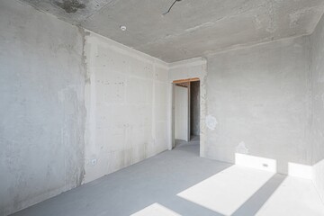 Bare, light-filled room in renovation with exposed concrete ceiling, plastered walls, and smooth concrete floor