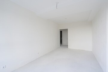 empty, all-white room with a doorway leading to another space. The walls are plain, and the floor is bare. Minimalist and clean aesthetic.