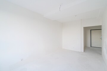 empty, all-white room with a doorway leading to another space. The walls are plain, and the floor is bare. Minimalist and clean aesthetic.