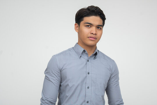 Young Southeast Asian man looking uneasy and slightly awkward, with a tense expression and body posture. Isolated on a light background.