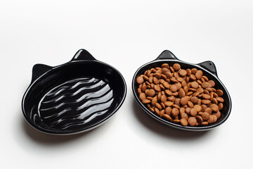 Two black bowls with ears, in shape, one is empty, the other is filled with dry food.