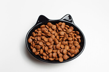 Dry food in black ceramic bowl in shape of cat with ears, isolated on white background.