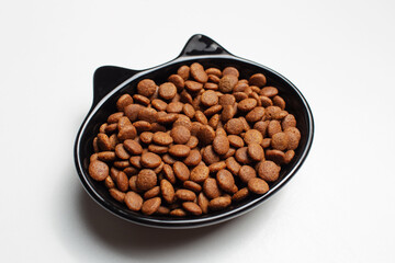 Dry food in black ceramic bowl in shape of cat with ears, isolated on white background.