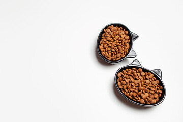 Dry food in black ceramic bowl in shape of cat with ears, isolated on white background.