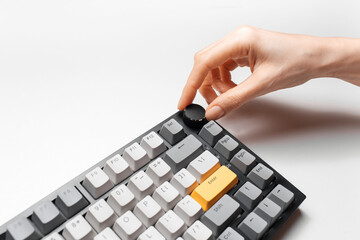 Female hand adjusting volume control on keyboard with yellow and grey key cap, on white background.