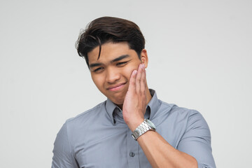 Southeast Asian man touching his cheek with a pained expression, suggesting toothache or facial discomfort. Isolated on a light background.