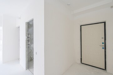 empty, all-white room with a doorway leading to another space. The walls are plain, and the floor is bare. Minimalist and clean aesthetic.